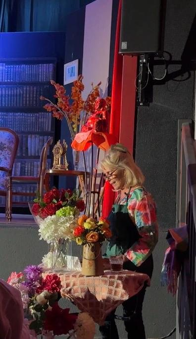 Une femme souriante devant une table couverte de bouquets de fleurs, à côté du décor